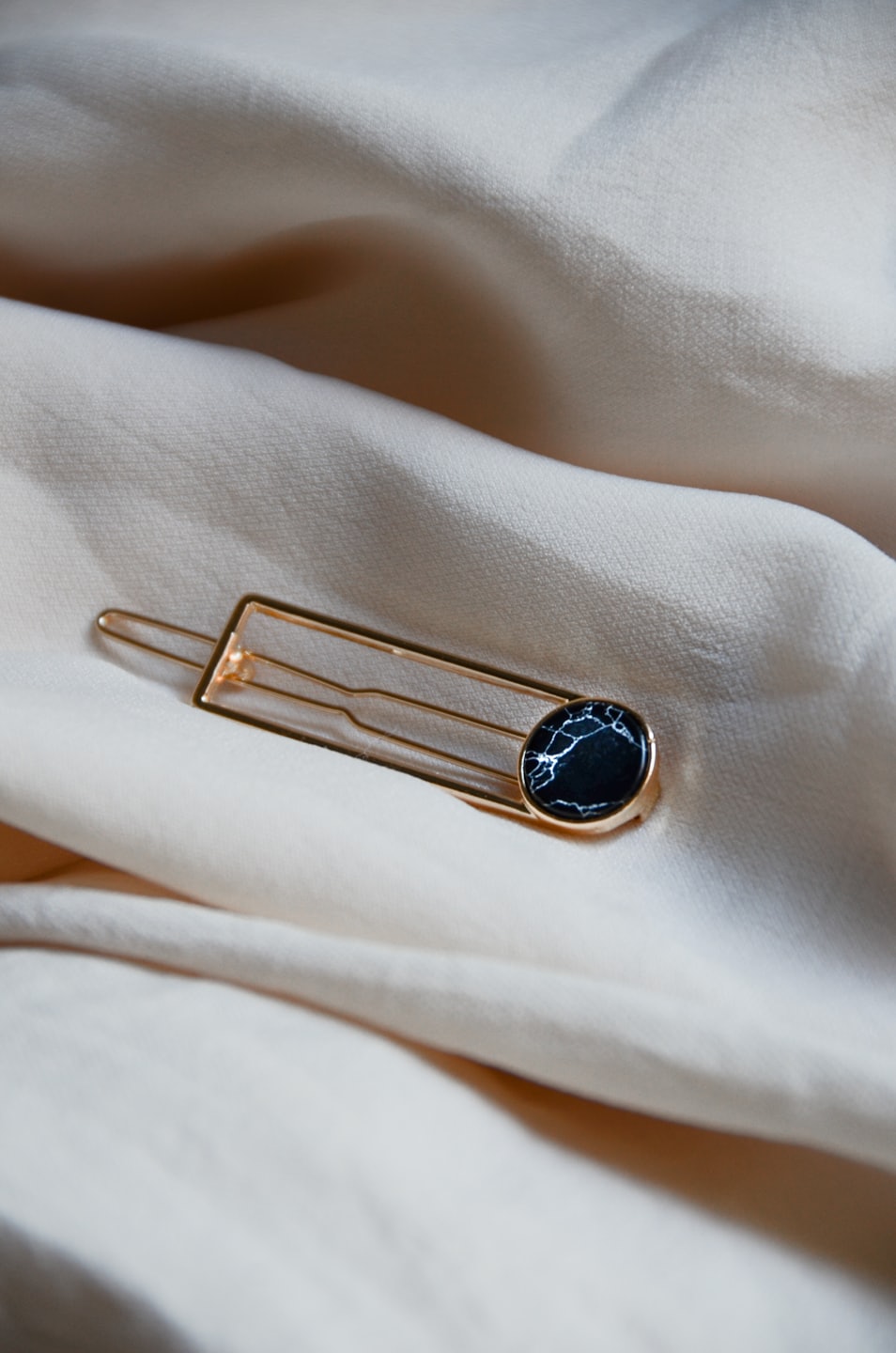 Gold hair clip with black marbled stone on cream fabric.