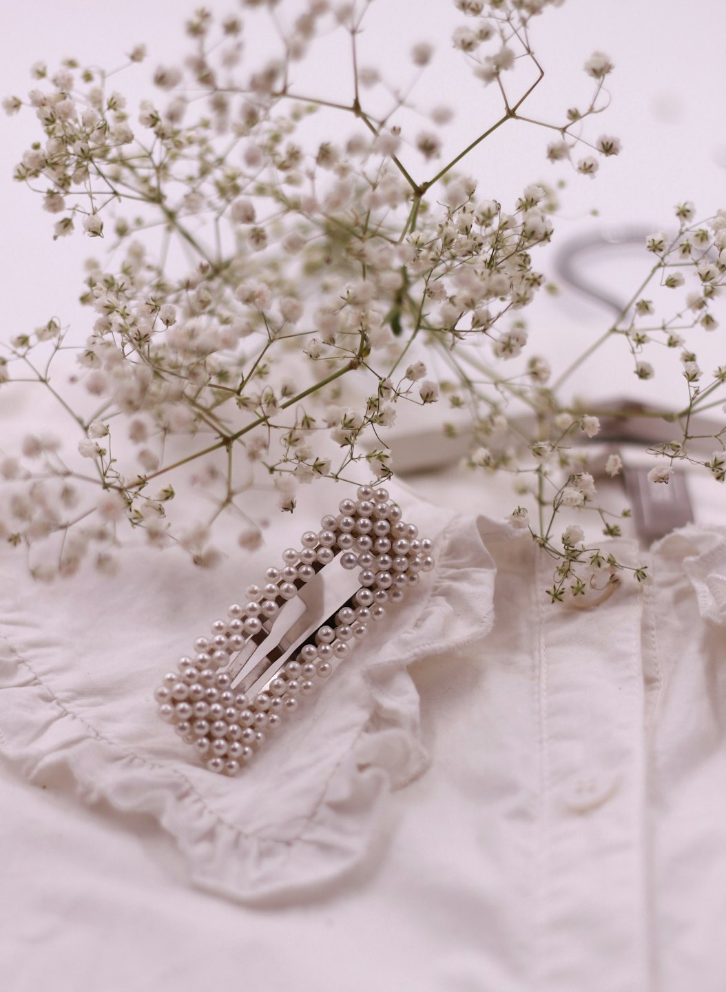 Pearl hair clip on a white ruffled blouse collar.