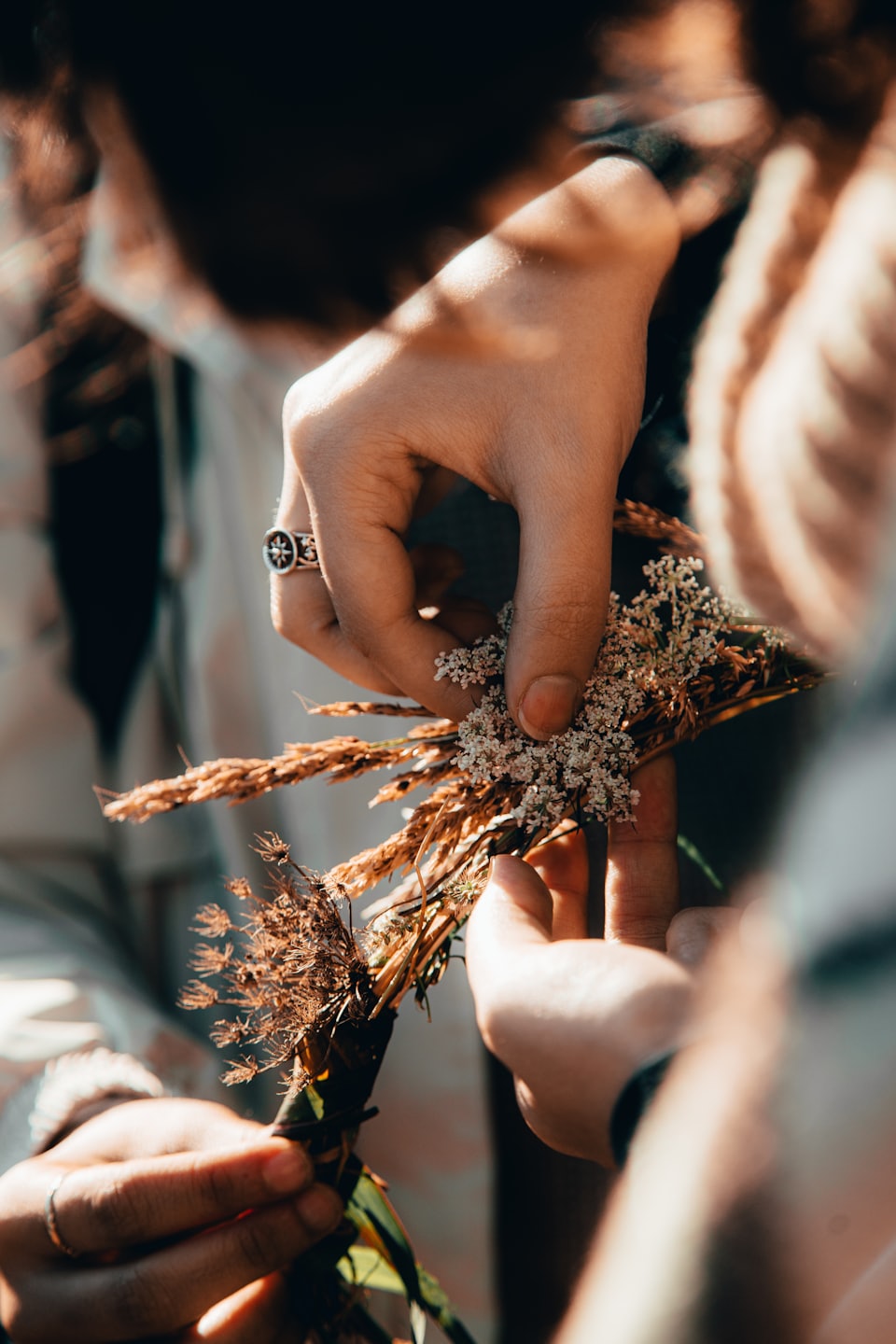 Hands arranging white flowers and dried grasses into a craft.